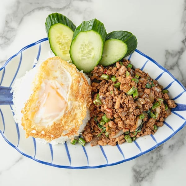 Thai basil chicken with a fried egg, rice, and cucumber slices on a striped plate.