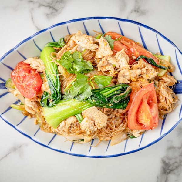 Glass noodles with chicken, bok choy, tomatoes, and cilantro in a blue and white bowl.