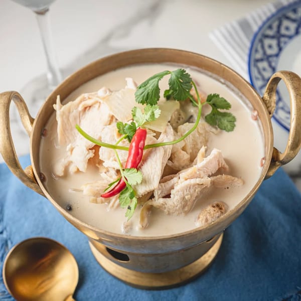 Creamy Thai coconut soup with chicken, cilantro, and red chili in a brass pot.