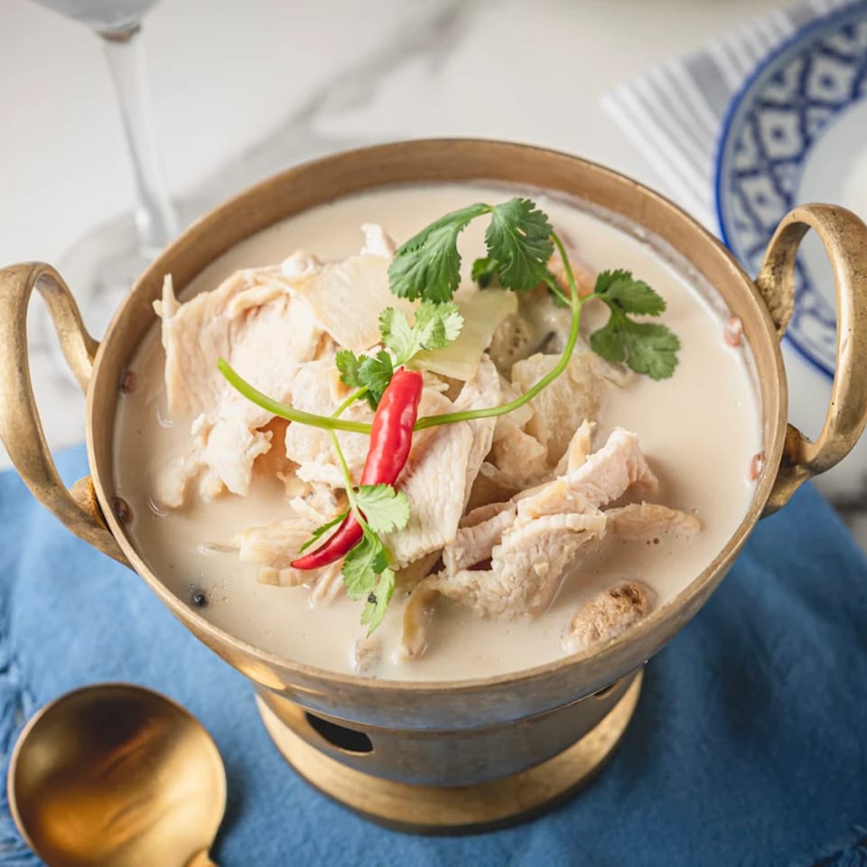 Creamy Thai coconut soup with chicken, cilantro, and red chili in a brass pot.