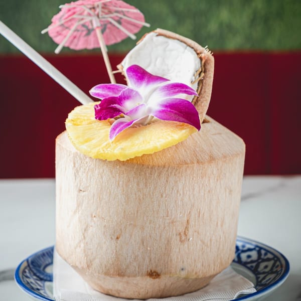 Fresh coconut drink garnished with pineapple, a purple orchid, and a pink umbrella.