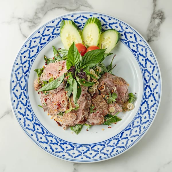 Thai beef salad with fresh herbs, chili flakes, and cucumber on a decorative plate.